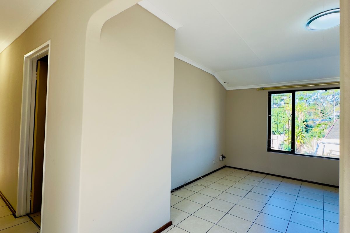 A bright, empty living area featuring neutral tiled flooring, coved ceilings, and a window with security bars, offering a clean canvas for interior design.