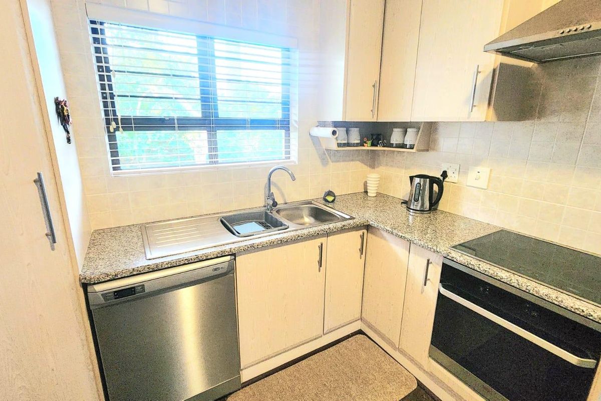A functional kitchen featuring granite countertops, built-in cabinetry, a stainless steel sink, and integrated appliances including an oven, hob, and dishwasher.