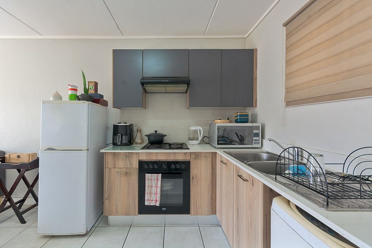 Compact kitchen featuring wood-look lower cabinetry, dark grey upper cabinets, integrated oven and hob, and tiled flooring.