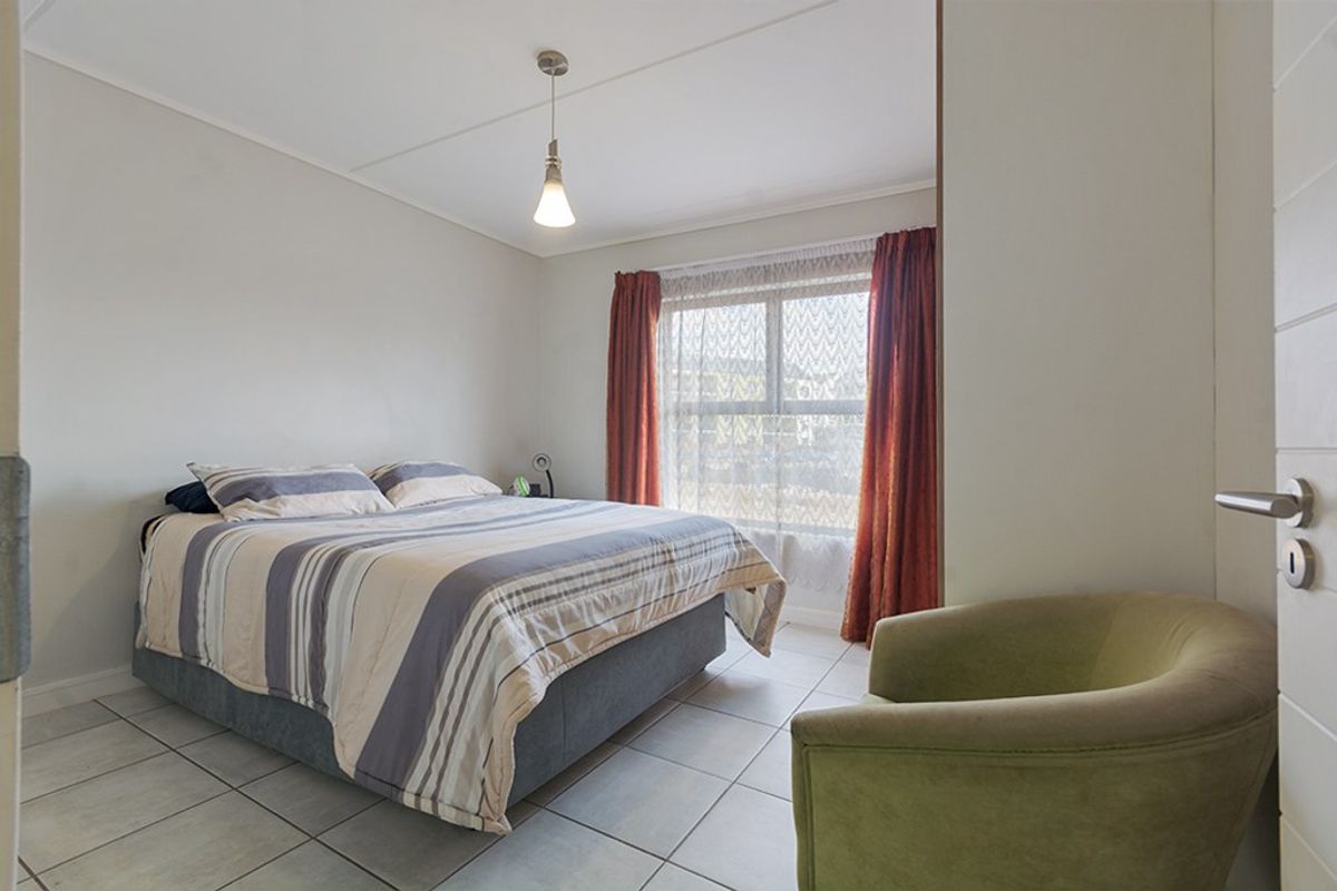 A functional bedroom featuring tiled flooring, a central pendant light, and a window with curtains, providing a neutral space for rest.