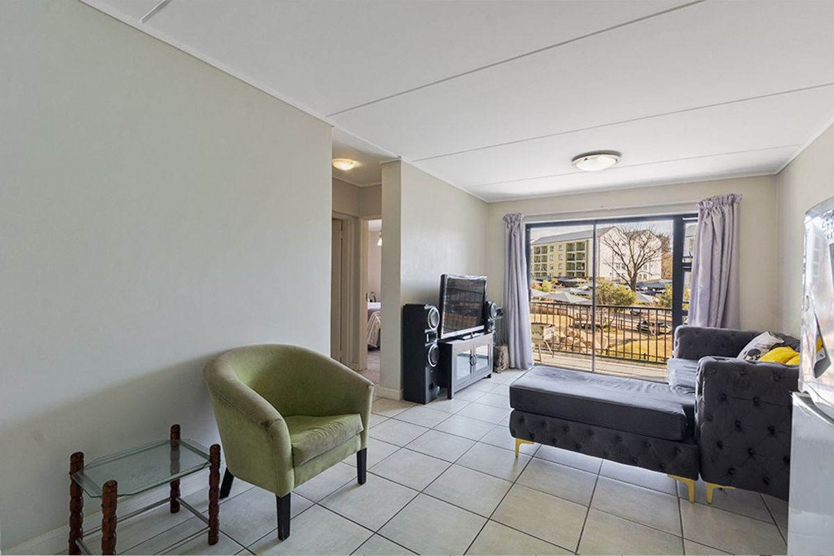 A bright living room featuring tiled flooring and a large sliding glass door that provides access to an outdoor balcony area.