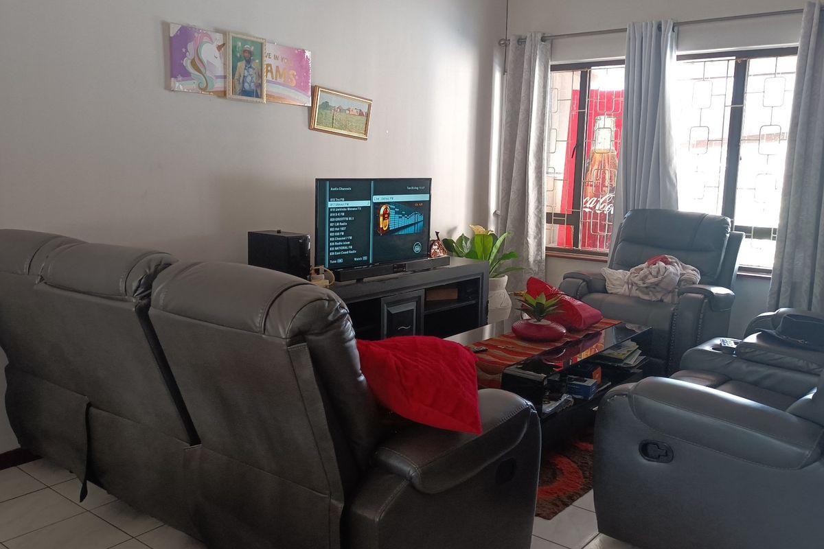 A comfortable living room featuring tiled flooring and large windows fitted with security bars and curtain rails.