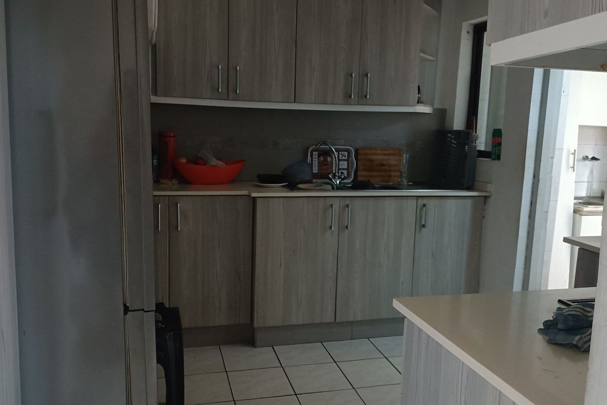 A functional kitchen featuring light wood-grain laminate cabinetry, tiled flooring, and integrated sink area with ample storage space.