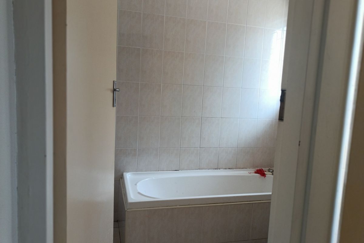 A functional bathroom featuring a built-in bathtub with neutral ceramic wall tiling.