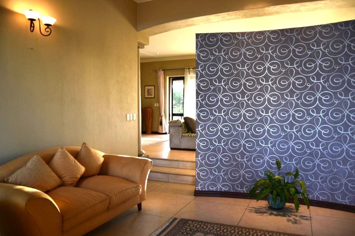 A living area featuring a decorative patterned feature wall, tiled flooring, and a stepped transition leading to an adjacent room.