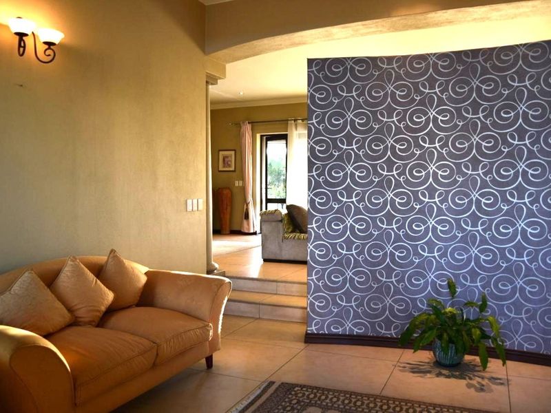 A living area featuring a decorative patterned feature wall, tiled flooring, and a stepped transition leading to an adjacent room.