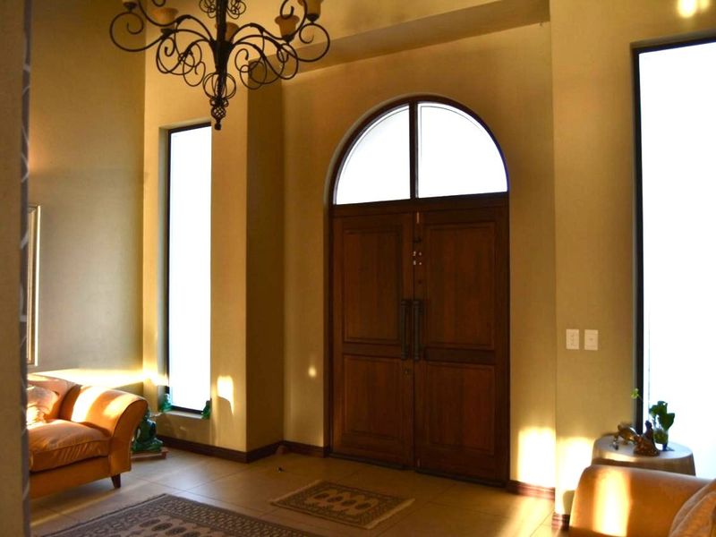 Spacious entrance foyer featuring double timber doors, an arched transom window, tall side windows, and a decorative wrought iron chandelier.