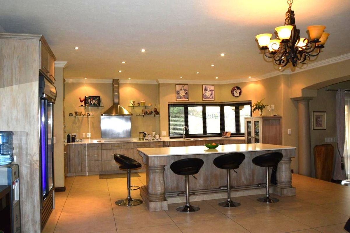 Spacious kitchen featuring a large central island with stone countertops, stainless steel extractor fan, ample cabinetry, and recessed lighting throughout.
