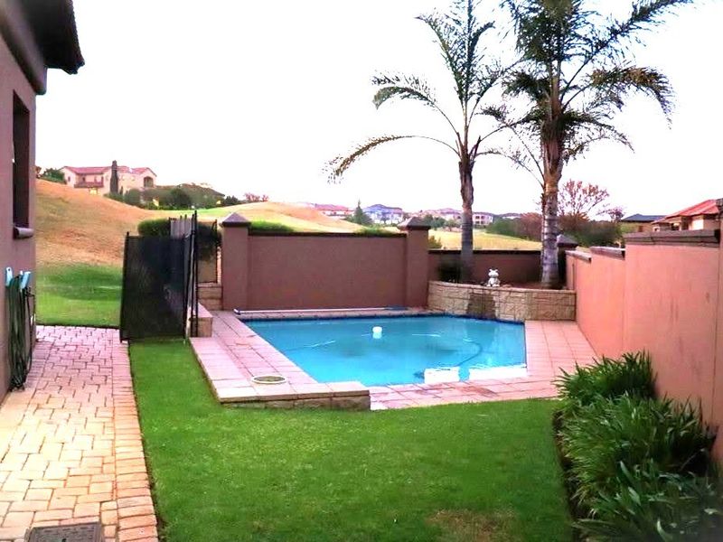 A private backyard featuring a swimming pool with paved surround, landscaped garden, and boundary walls, overlooking a scenic golf course landscape.