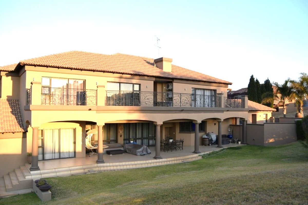 Rear elevation of a double-story house featuring a spacious covered patio, upper-level balcony with wrought iron railings, and large sliding doors.