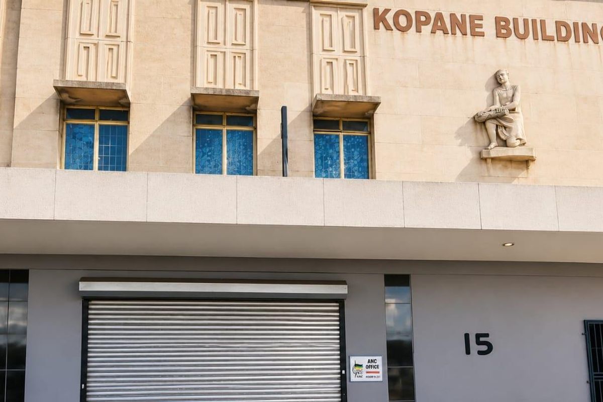 Front facade of the Kopane Building featuring a roller shutter entrance, decorative stone sculpture, and prominent building signage.