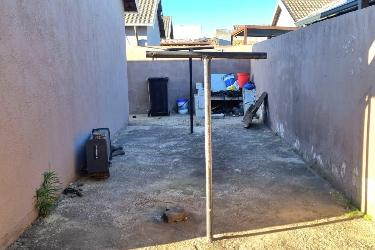 A narrow rear exterior courtyard featuring concrete paving and boundary walls, suitable for a utility or garden space renovation.