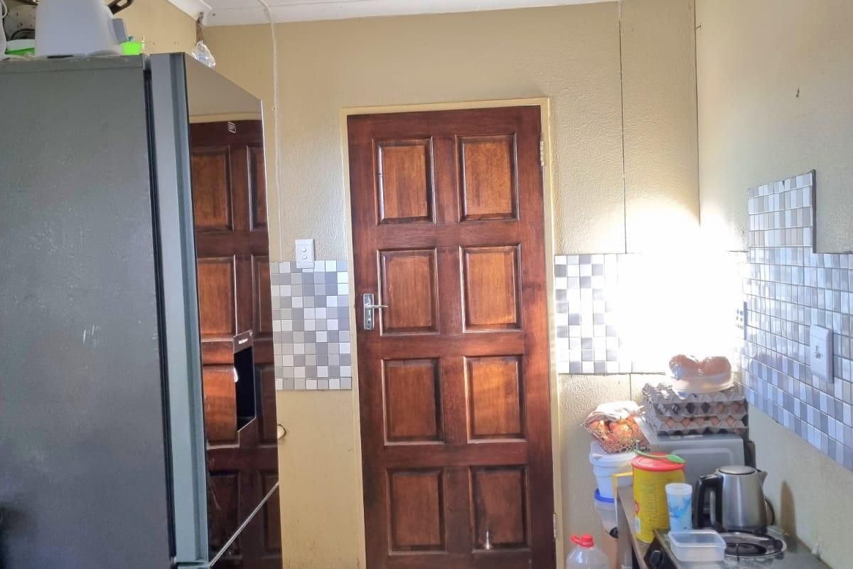 A compact kitchen area featuring tiled flooring, a tiled splashback, and a traditional timber door, requiring cosmetic updates to improve its overall condition.
