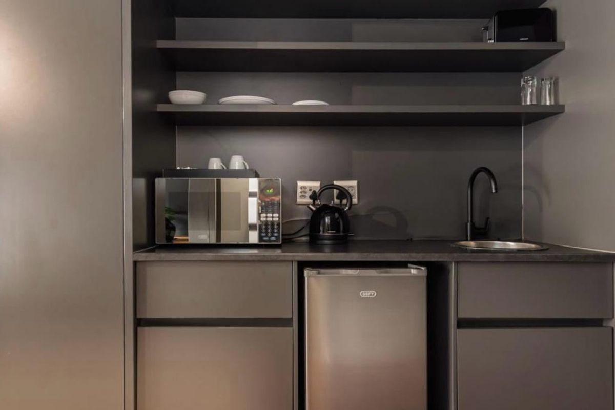 A compact, modern scullery or kitchenette area featuring sleek dark cabinetry, open shelving, a small sink with a matte black faucet, and integrated storage.