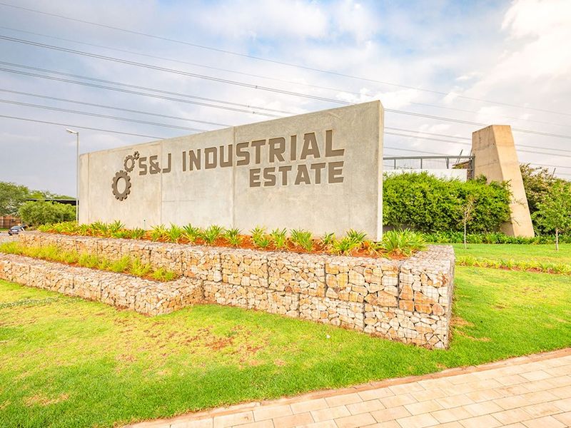 A well-maintained entrance signage wall for S&J Industrial Estate, featuring modern concrete construction, gabion stone retaining walls, and manicured landscaping.