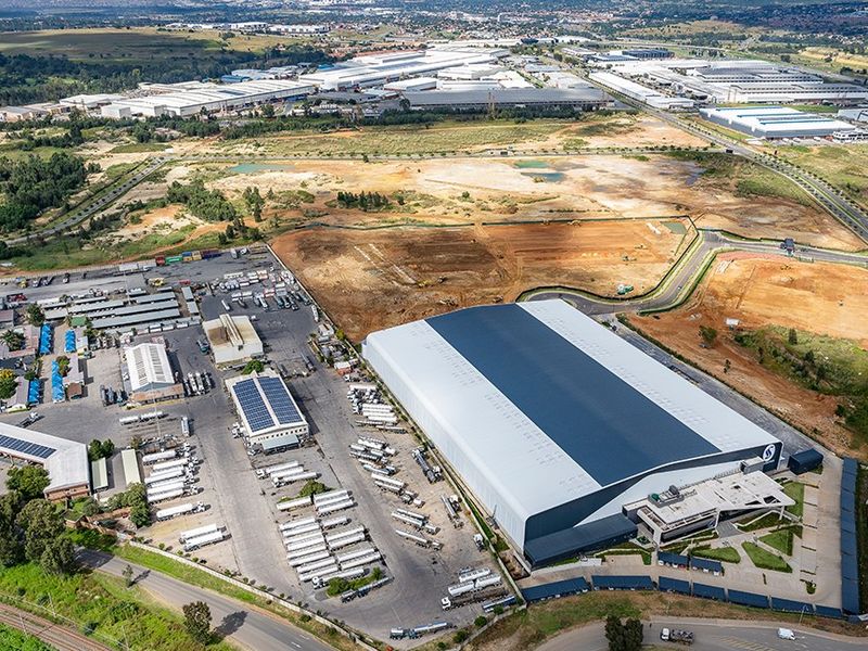 Aerial view of a large commercial industrial facility featuring a warehouse, extensive logistics yard, solar installations, and surrounding infrastructure.