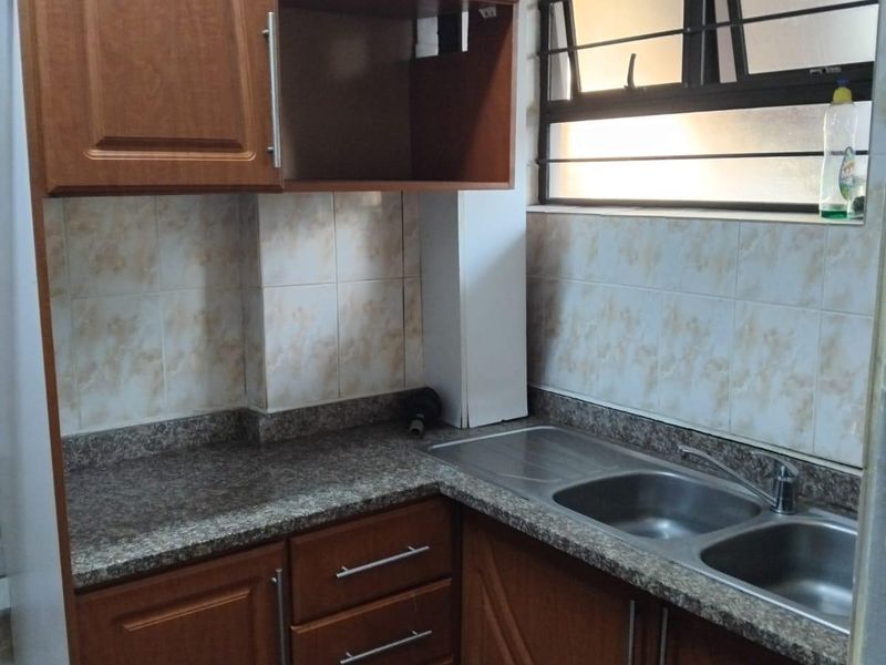 Compact kitchen featuring wood-look cabinetry, granite countertops, a double stainless steel sink, and tiled backsplash with security bars on the window.