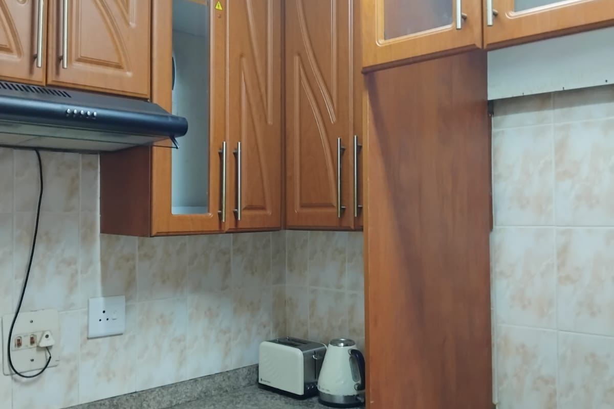 A functional kitchen featuring traditional wooden cabinetry, granite countertops, a built-in electric hob, oven, and extractor fan with a tiled backsplash.