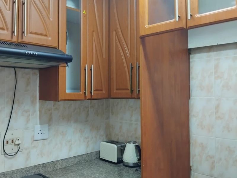 A functional kitchen featuring traditional wooden cabinetry, granite countertops, a built-in electric hob, oven, and extractor fan with a tiled backsplash.