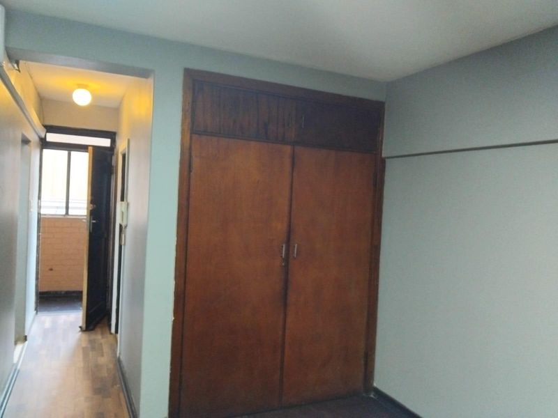 A bedroom featuring a built-in wooden wardrobe, laminate flooring, and neutral wall tones, offering a functional space ready for personalization.