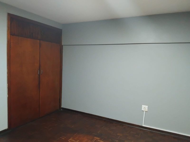 An empty bedroom featuring original parquet flooring and a built-in wooden wardrobe, offering a blank canvas for renovation or interior design updates.