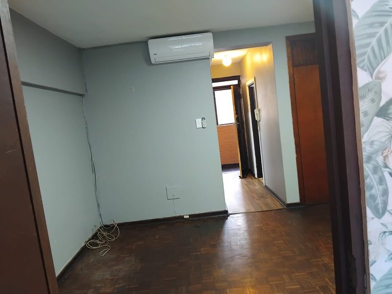 An empty living area featuring parquet flooring, a wall-mounted air conditioning unit, and access to a hallway.
