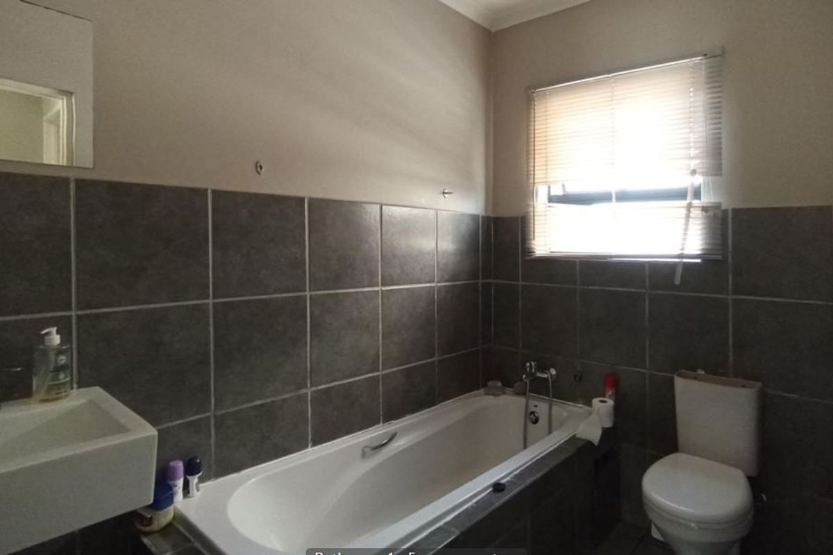 A functional bathroom featuring a built-in bathtub, wall-mounted basin, toilet, and neutral tiled wall finishes.