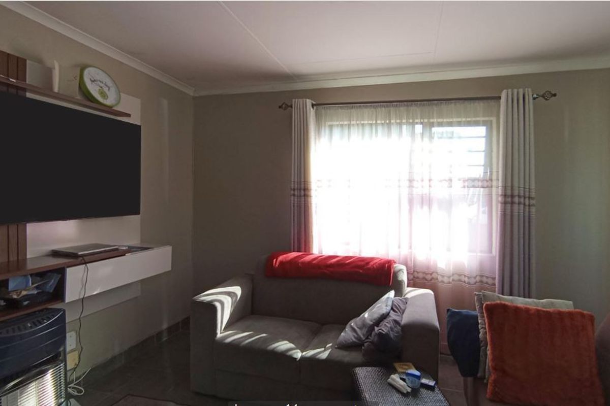 A comfortable living room featuring a built-in media unit, tiled flooring, and natural light through a window with fitted curtains.