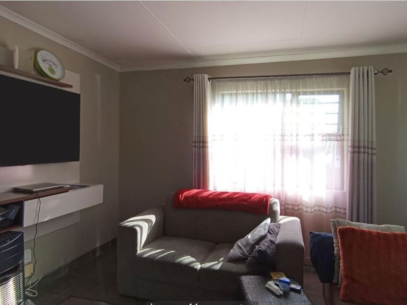 A comfortable living room featuring a built-in media unit, tiled flooring, and natural light through a window with fitted curtains.