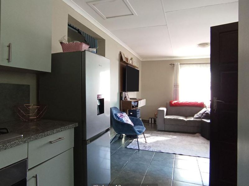 Open-plan living area featuring a compact kitchen with built-in cabinetry and gas hob, flowing into a comfortable lounge space with tiled flooring.