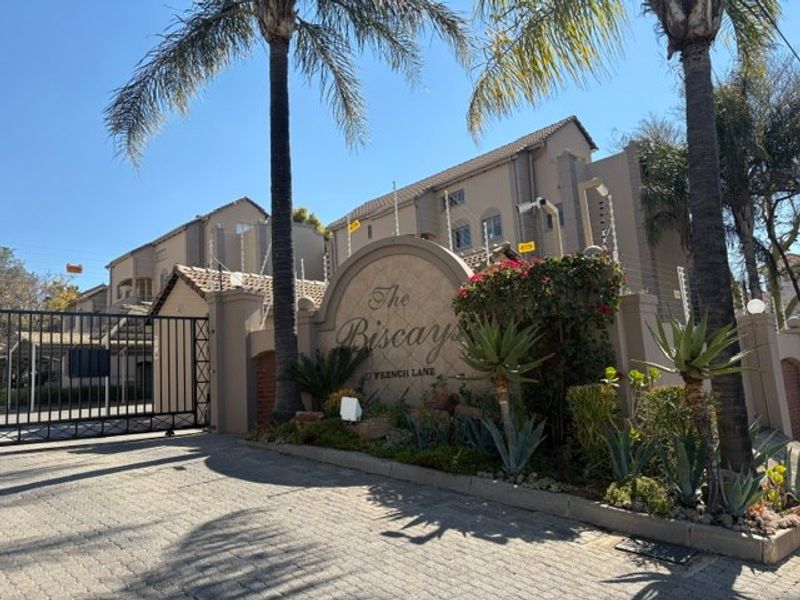 Front entrance view of The Biscays apartment complex, featuring a secure gated access point, paved driveway, and established perimeter landscaping.