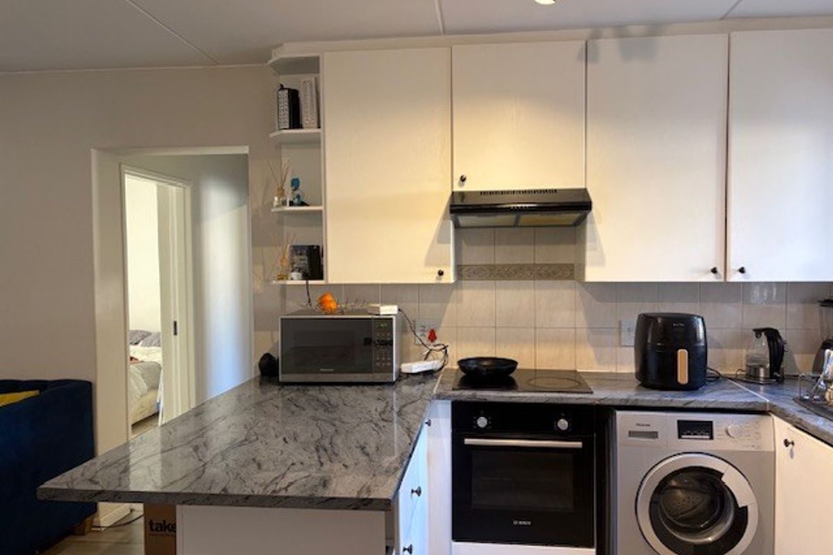 Functional kitchen featuring stone countertops, built-in oven, electric hob, extractor fan, and integrated washing machine with ample cabinetry.