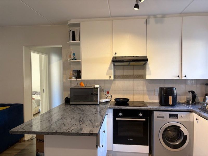 Functional kitchen featuring stone countertops, built-in oven, electric hob, extractor fan, and integrated washing machine with ample cabinetry.