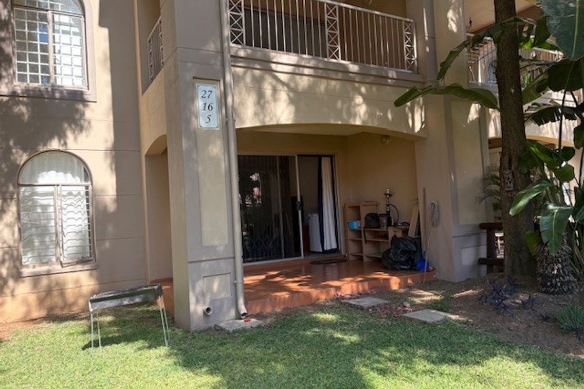 Ground floor apartment exterior featuring a tiled patio, sliding glass doors, and an upper-level balcony with metal railings.