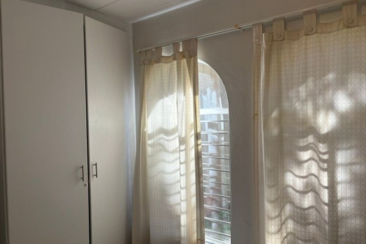 A bedroom featuring a built-in wardrobe and an arched window with security bars, providing natural light.