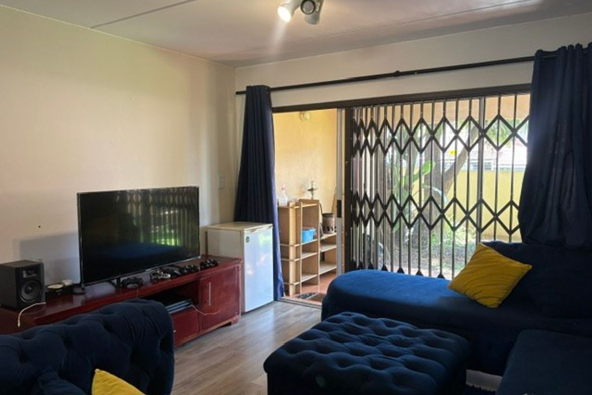A living room featuring laminate flooring and a sliding glass door with a security gate, providing access to an outdoor area.