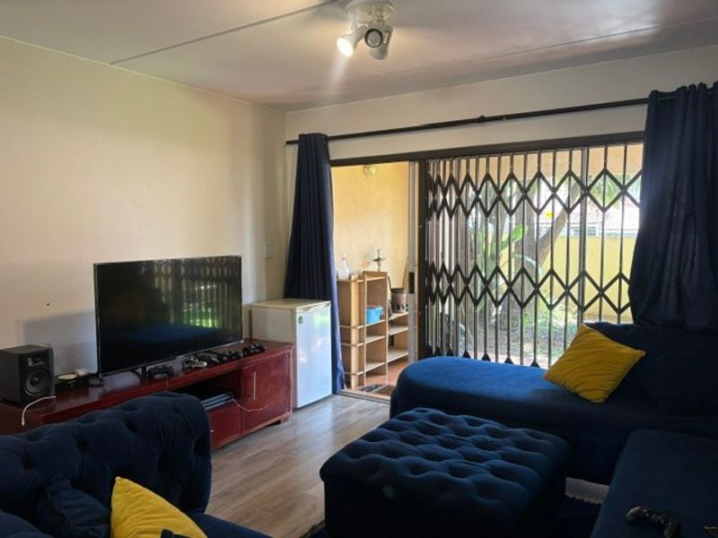 A living room featuring laminate flooring and a sliding glass door with a security gate, providing access to an outdoor area.