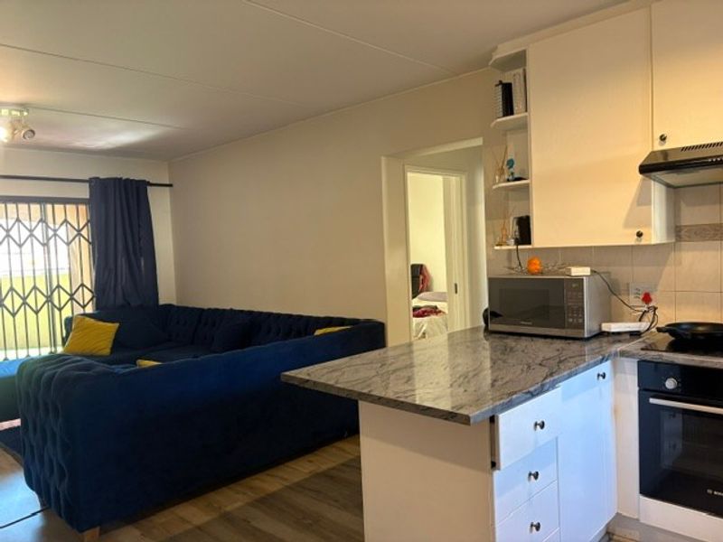 Open-plan living area featuring a kitchen with granite countertops, built-in oven, and extractor fan, seamlessly flowing into the lounge space with security gate access.