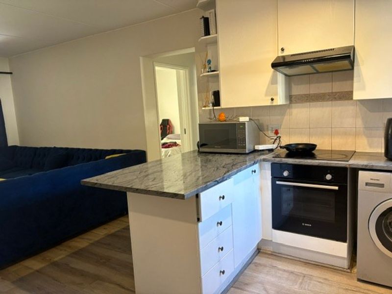 Open-plan kitchen featuring stone countertops, built-in oven, electric hob, and extractor fan, seamlessly integrated with the living area.
