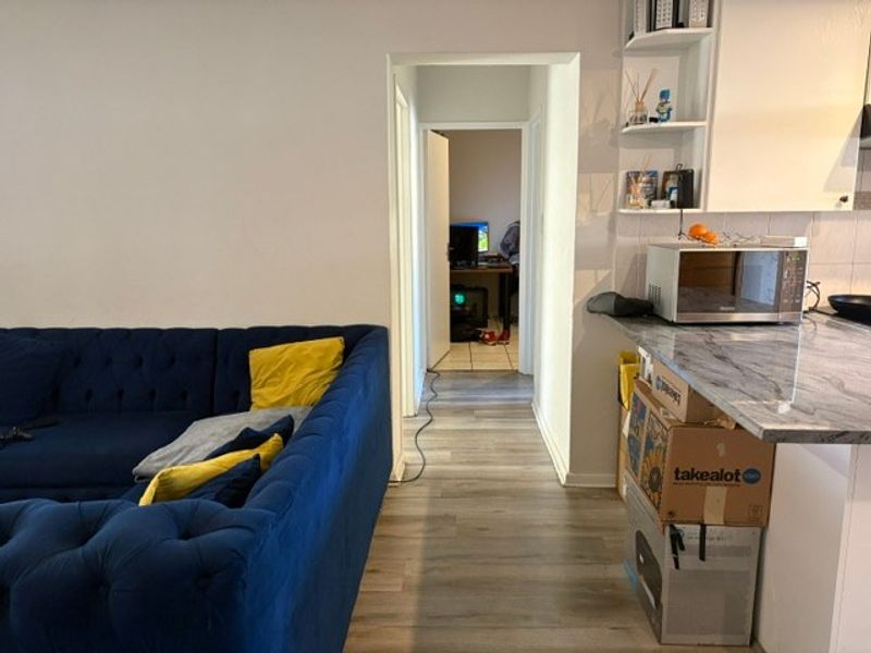 Open plan living area featuring laminate flooring, a stone-look kitchen countertop, and built-in shelving, leading into a hallway.