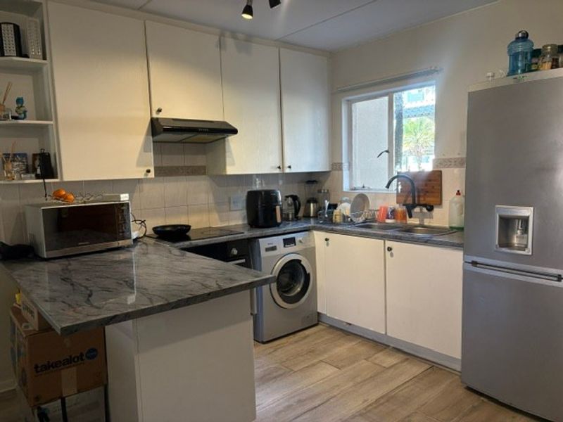 Functional kitchen featuring white cabinetry, stone-look countertops, integrated oven, extractor fan, and wood-look floor tiles with a convenient laundry connection.