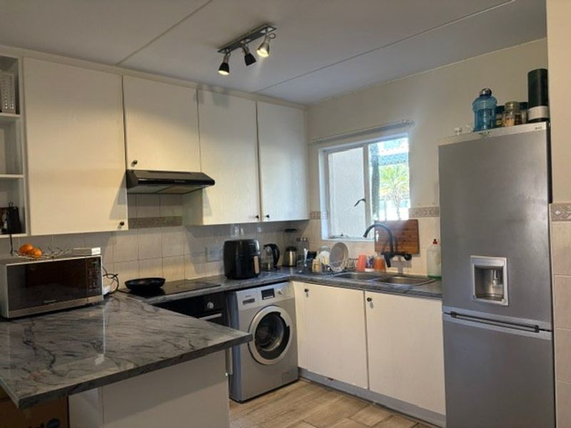A functional kitchen featuring white cabinetry, stone-look countertops, integrated washing machine, and tiled backsplash with modern track lighting.