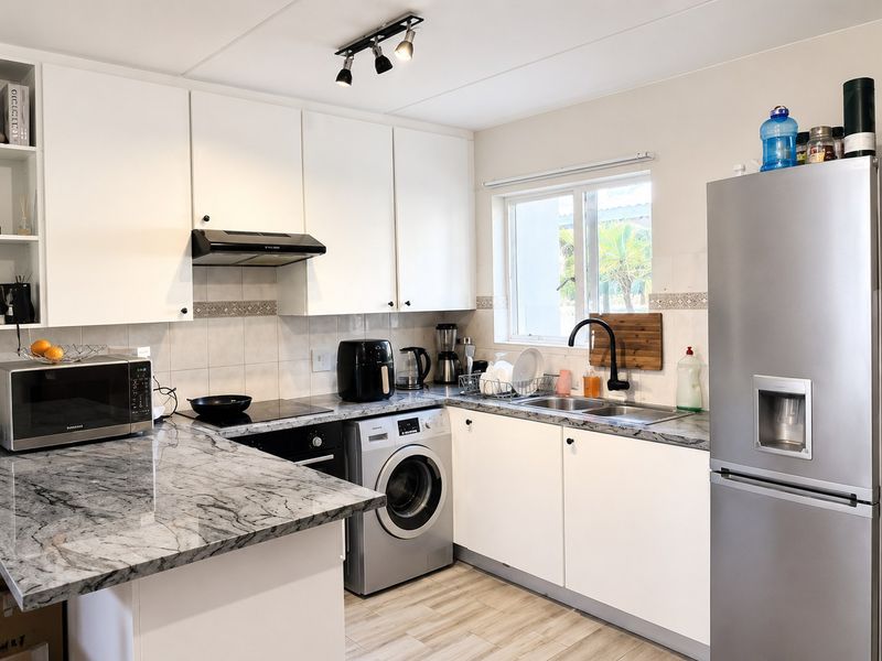 A functional kitchen featuring white cabinetry, marble-look countertops, a stainless steel sink, built-in oven, hob, extractor fan, and an integrated washing machine.