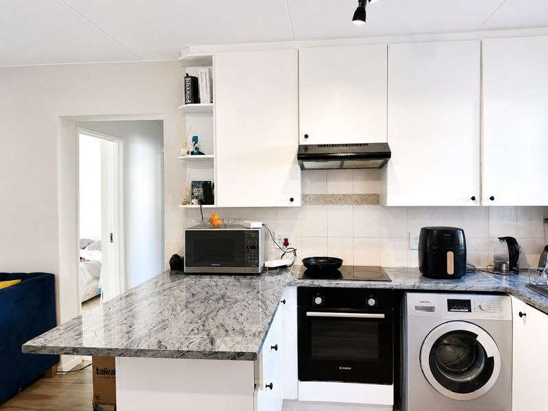 Modern kitchen featuring granite countertops, built-in oven, electric hob, extractor fan, and an integrated washing machine with ample cabinetry.