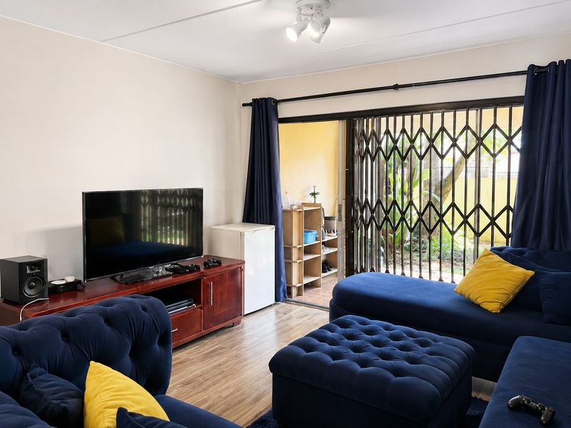 A well-maintained living room featuring laminate flooring, a ceiling spotlight, and a sliding glass door with a security gate leading to an outdoor area.