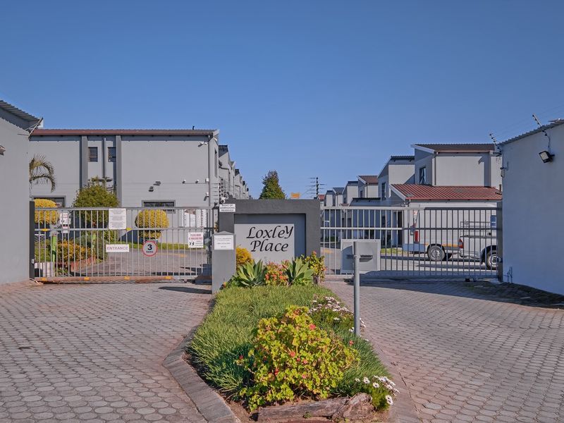 The secure entrance to Loxley Place apartment complex, featuring a gated access point, paved driveway, and well-maintained perimeter security fencing.