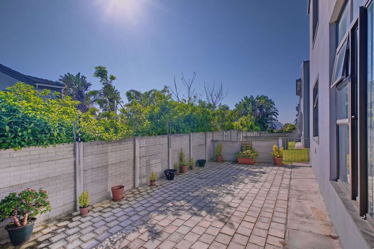 A private rear paved patio area featuring a precast concrete boundary wall with integrated electric fencing and a metal access gate.