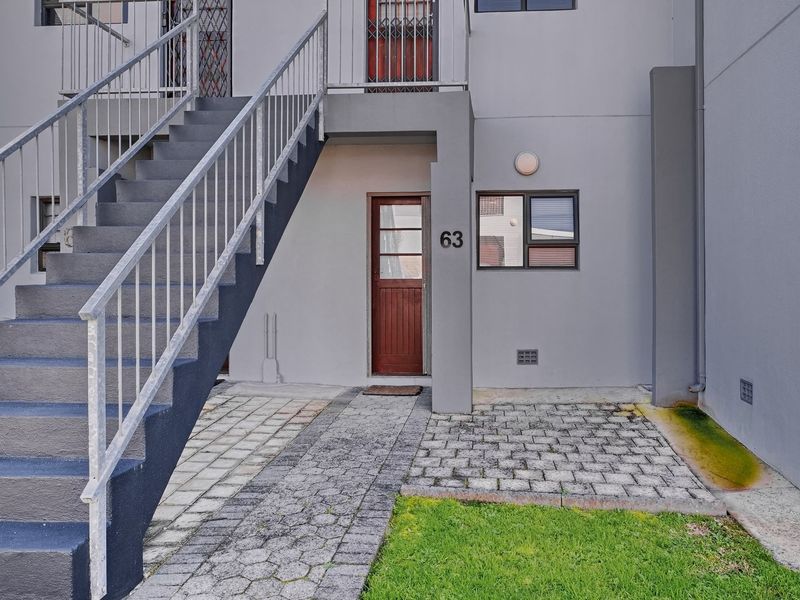 Front entrance of the apartment featuring a paved walkway, external staircase with metal railing, and a secure wooden door.