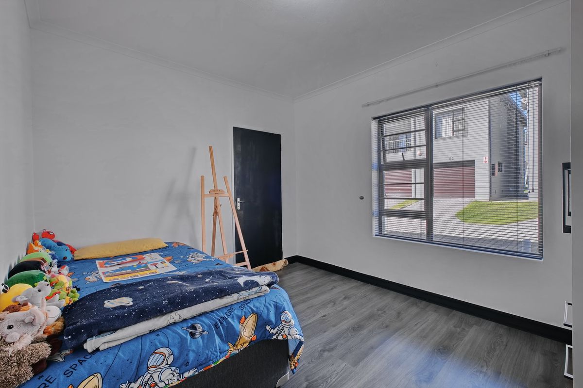 A well-maintained bedroom featuring modern grey laminate flooring, white walls, and an aluminium-framed window with venetian blinds.