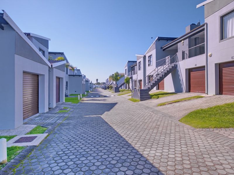 A view of a residential apartment complex street featuring paved driveways, roller garage doors, and external staircases leading to upper-level units.